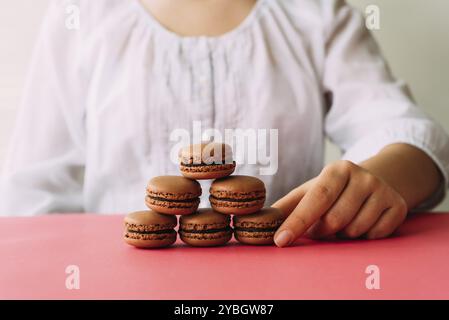 Woman placing macarons on heap on pink table. Selective focus Stock Photo