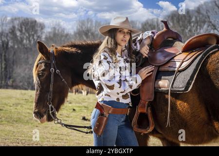 A beautiful brunette cowgirl poses with her horse before riding in the country Stock Photo