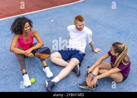 Multi-ethnic friends sitting on the ground relaxed and talking in a pickelball court Stock Photo