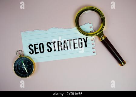 SEO Strategy text written on paper torn with compass and magnifying glass top view on pink background Stock Photo