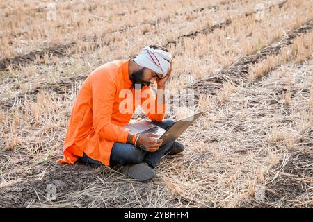 Indian rural farmer working on laptop in field of crops Stock Photo