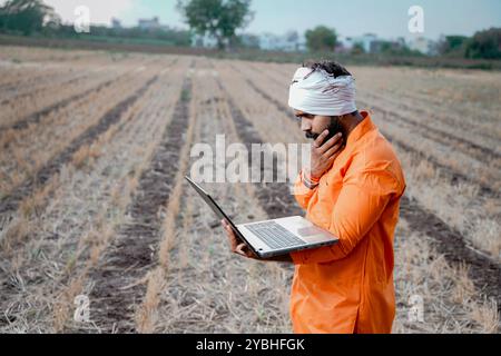 Indian rural farmer working on laptop in field of crops Stock Photo