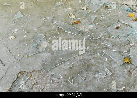 Pieces of broken glass lie on the concrete surface. A large number of shards of transparent glass lie on the ground Stock Photo