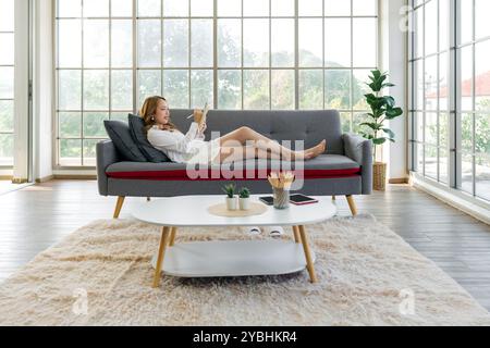 Young asian woman is relaxing on a comfortable sofa, smiling while writing down her to-do list in  living room at home. Stock Photo