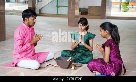 An Indian family in traditional attire performs a Yagya or Havan, led by a priest, to balance energies in their home. This sacred pooja is for harmony Stock Photo