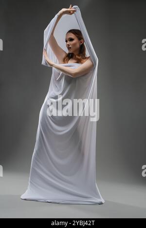 Model elegantly poses with flowing white fabric in a studio setting Stock Photo