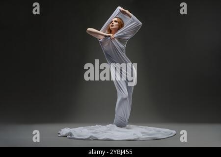 Model poses elegantly in a flowing gray garment against a dark backdrop Stock Photo