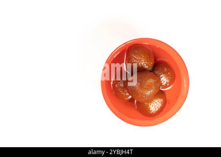 Top view of delicious Indian dessert gulab jamun in a vibrant red bowl against a white backdrop. Copy space for your text Stock Photo