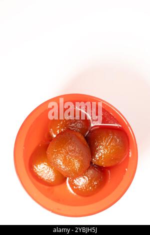 Top view of delicious Indian dessert gulab jamun in a vibrant red bowl against a white backdrop. Copy space for your text Stock Photo