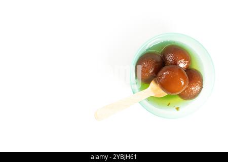Top view of delicious Indian dessert Gulab Jamun in a bowl served in sweet syrup with wooden spoon on white background. Stock Photo