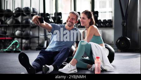 Fitness Couple In Gym Using Mobile Technology To Take Selfie Photo After Workout On Phone Stock Photo