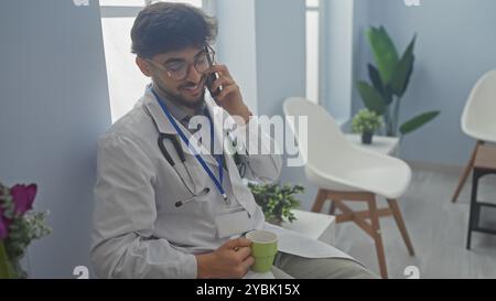 Handsome arab doctor in white coat with stethoscope talking on phone in hospital lobby. Stock Photo