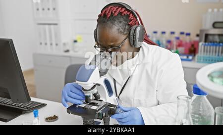 African american scientist with braids using microscope in laboratory Stock Photo