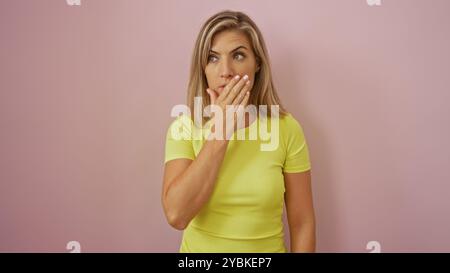 Beautiful blonde woman in a yellow shirt looking surprised against a pink background. Stock Photo