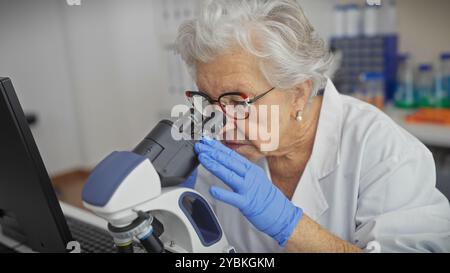 Senior woman scientist examining specimen through microscope in laboratory setting. Stock Photo