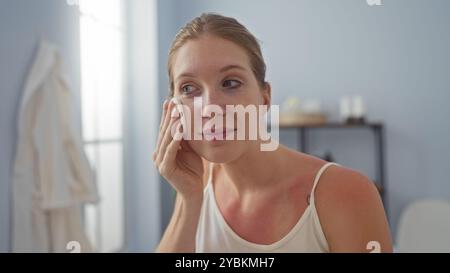 Woman applying makeup with a cotton pad in a serene spa room while enjoying a wellness session indoors Stock Photo