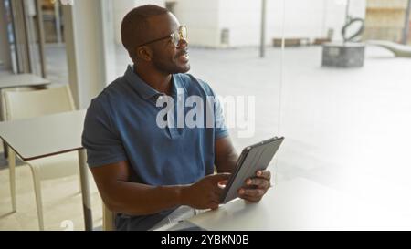 Young man in office holding tablet seated at table indoors with bright natural light Stock Photo