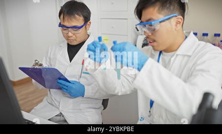 Two male scientists examining specimens in a laboratory, wearing white coats, gloves, and protective eyewear. Stock Photo