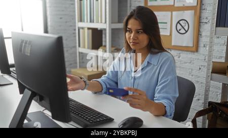 Woman holds credit card while working on computer in modern office environment showcasing technology and professional engagement Stock Photo