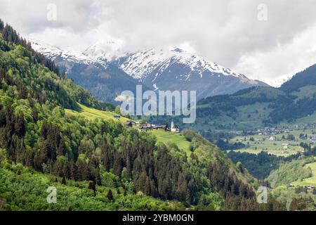 Sun shines over a mountainous village with snowed mountains and valleys in the background Stock Photo
