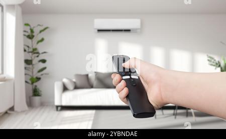 Hand holding a remote control, turning on or off an air conditioner in a cozy living room. Concept of home comfort, climate control, and modern techno Stock Photo