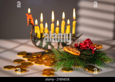 Christmukkah Celebration: Hanukkah Menorah with Burning Candles, Gelt, and Pine Branch. Christmas & Hanukkah Stock Photo