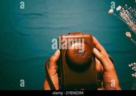 Madrid, Spain. 1 May 2023 Vintage Leica camera in brown leather case lying in female hands on blue background. Retro photography hobby. Photographer. Stock Photo