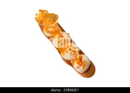 Sweet dessert eclairs or profiteroles with chocolate filling and covered with cream and dried oranges on a white background Stock Photo