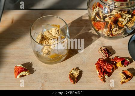 Preparation of fly agaric drink, ground powdered dry mushroom on ice cubes in a glass, illuminated by natural sunlight.  Homemade fly agaric elixir. Stock Photo