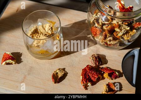 Preparation of fly agaric drink, ground powdered dry mushroom on ice cubes in a glass, illuminated by natural sunlight.  Homemade fly agaric elixir. Stock Photo