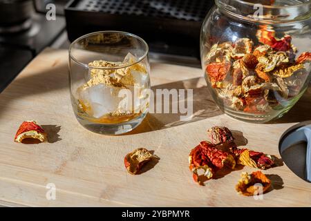 Preparation of fly agaric drink, ground powdered dry mushroom on ice cubes in a glass, illuminated by natural sunlight.  Homemade fly agaric elixir. Stock Photo