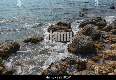 Small waves breaking on the coastal rocks form foam sparkling in the sun Stock Photo