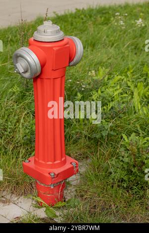 Bright red fire hydrant standing in green grass near a sidewalk on a sunny day Stock Photo