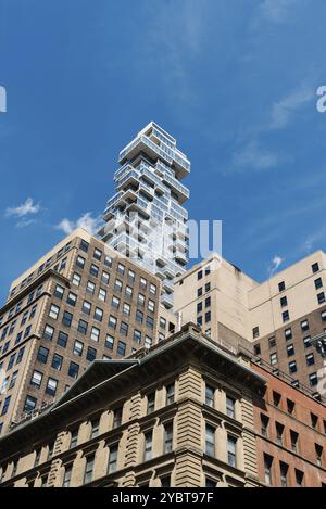 New York City, USA, June 25, 2018: Luxury New Apartment Building Emerging from Behind Old Buildings in Tribeca. Low angle view gainst blue sky. Vertic Stock Photo