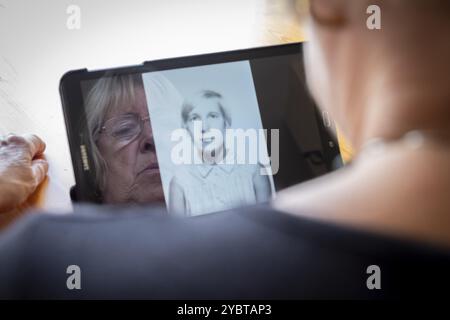 Senior caucasian woman looking at old photos of herself as a young woman on a tablet computer themes of contrasts the ageing process nostalgia and chi Stock Photo