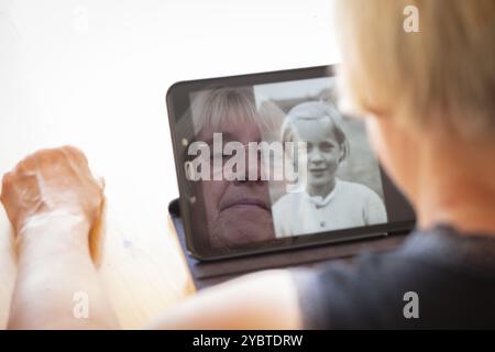 Senior caucasian woman looking at old photos of herself as a young woman on a tablet computer themes of contrasts the ageing process nostalgia and chi Stock Photo