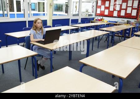 Primary school caucasian girl using a laptop in an empty classroom Stock Photo