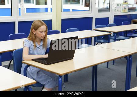 Primary school caucasian girl using a laptop in an empty classroom Stock Photo