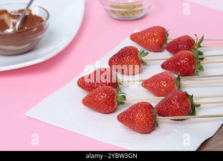 Strawberries on sticks on white plate. Process of cooking berries in chocolate.  Stock Photo