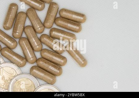 Closeup of brown pills lying next to euro coins on a white background symbolizing expensive healthcare costs Stock Photo