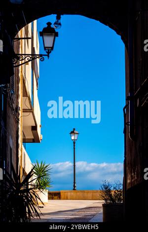 View of a lamplight framed by an archway in Via Venezia, Bari, Italy, with a bright blue sky and clouds in the background. Stock Photo