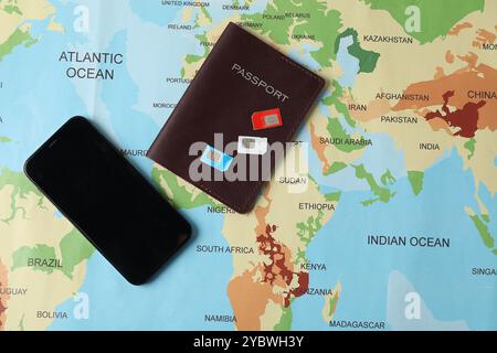 SIM cards, smartphone and passport on world map, flat lay Stock Photo