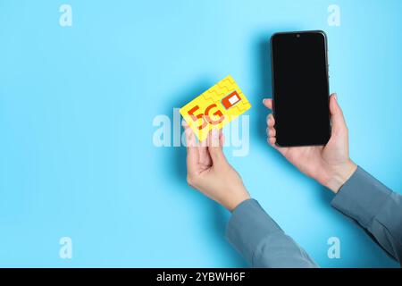 Woman holding 5G SIM card and smartphone on light blue background, closeup. Space for text Stock Photo