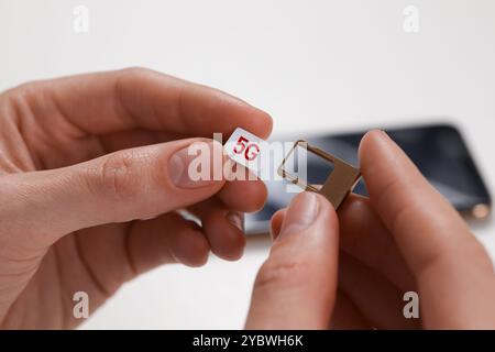 Woman with 5G SIM card and slot tray on white background, closeup Stock Photo