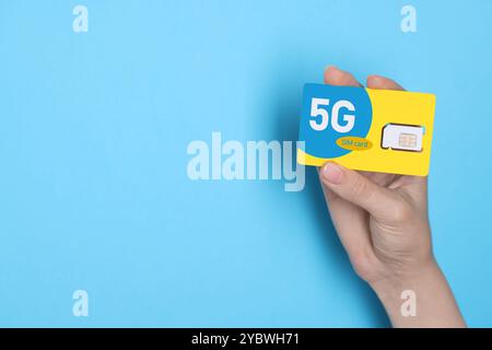 Woman holding 5G SIM card on light blue background, closeup. Space for text Stock Photo