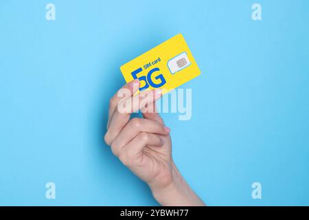 Woman holding 5G SIM card on light blue background, closeup Stock Photo