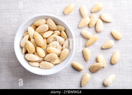 Freshly blanched almonds in white bowl on linen. Shelled almonds that have been treated with hot water to soften the seed coat, which is then removed. Stock Photo