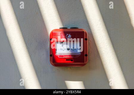 Red fire alarm box with arrows symbolizing emergency activation system on beige wall hotel under sunlight. Greece. Stock Photo