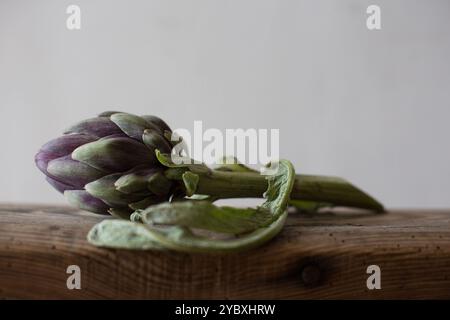 Fresh globe artichoke resting on a rustic wooden surface, natural light highlighting its textured leaves. Stock Photo