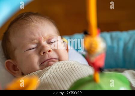 Crying baby boy in beige attire, showing emotion and curiosity in play area. Stock Photo